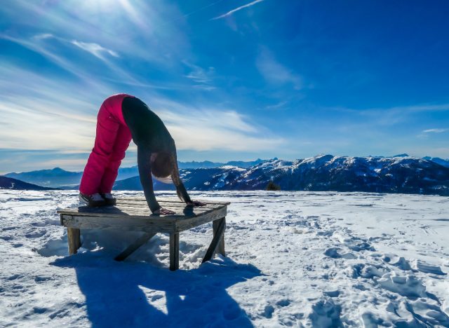 woman stretching on snowy slopes, demonstrating stretches to do after skiing