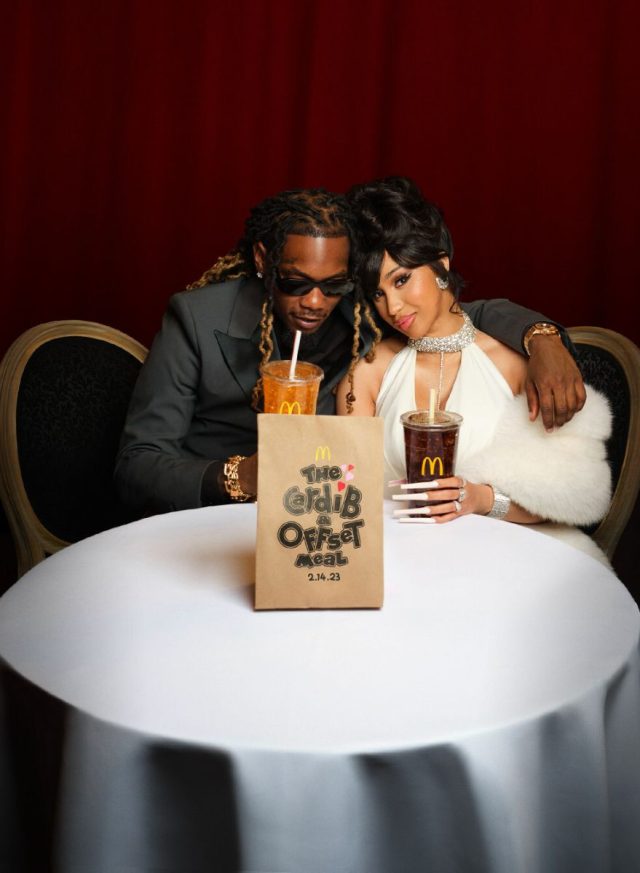 Rappers Offset and Cardi B sitting at a table with a McDonald's bag and drinks.