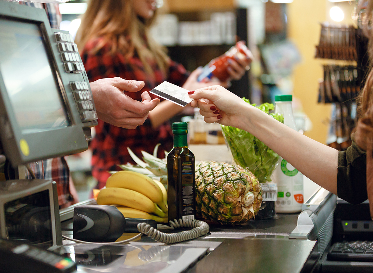 Cropped picture of young man gives credit card to cashier lady at workspace in supermarket.