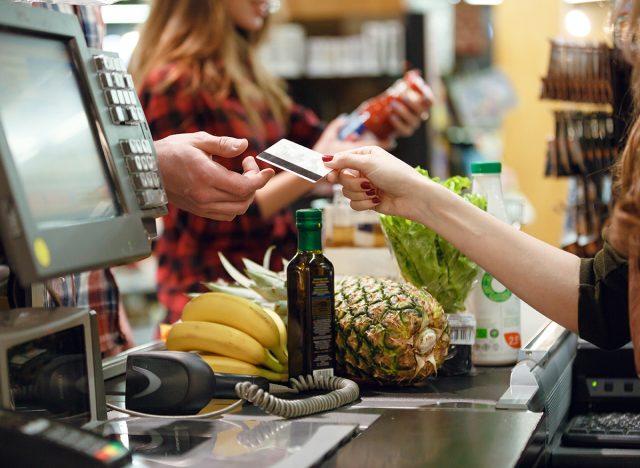 Cropped picture of young man gives credit card to cashier lady at workspace in supermarket.