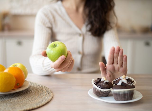 woman choosing healthy food like an apple over unhealthy junk food dessert