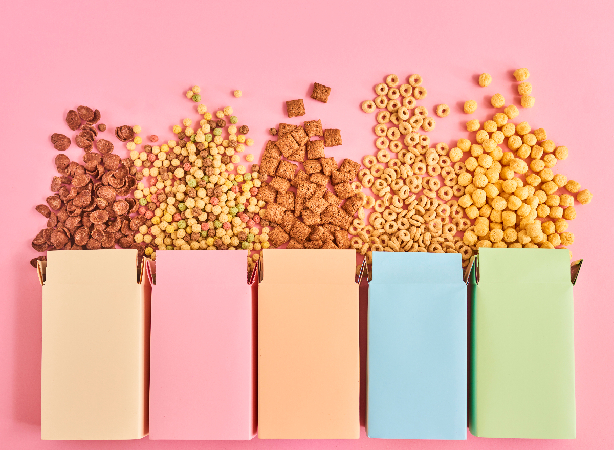 colorful boxes of breakfast cereals poured out onto pink background, concept of foods preventing you from losing weight