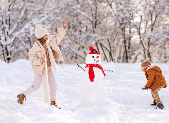 happy mother and son play in the snow next to snowman