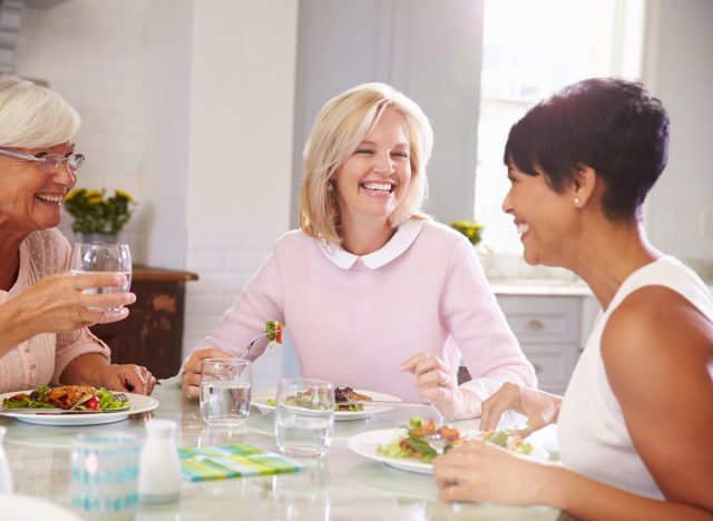 mature female friends laughing having lunch at one of their homes