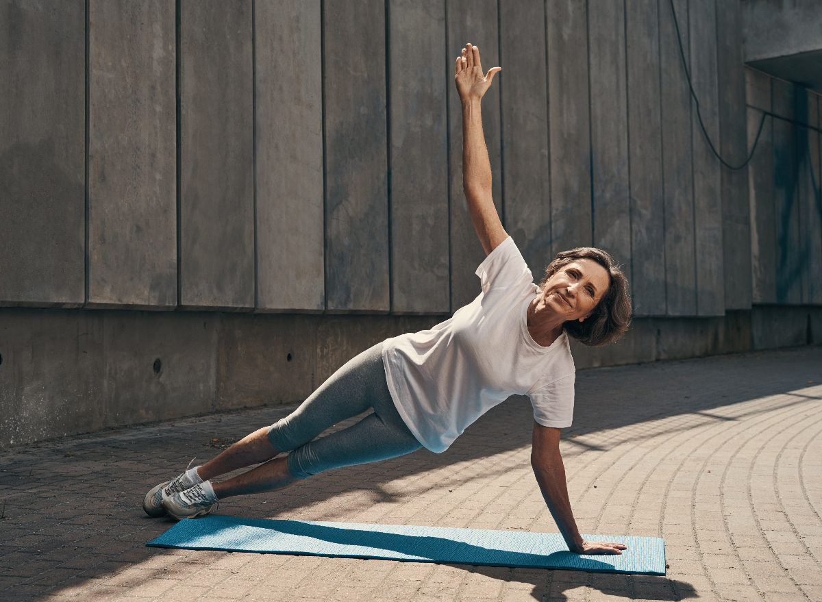 mature senior woman doing side plank exercise on yoga mat outdoors, core-strengthening exercises for seniors