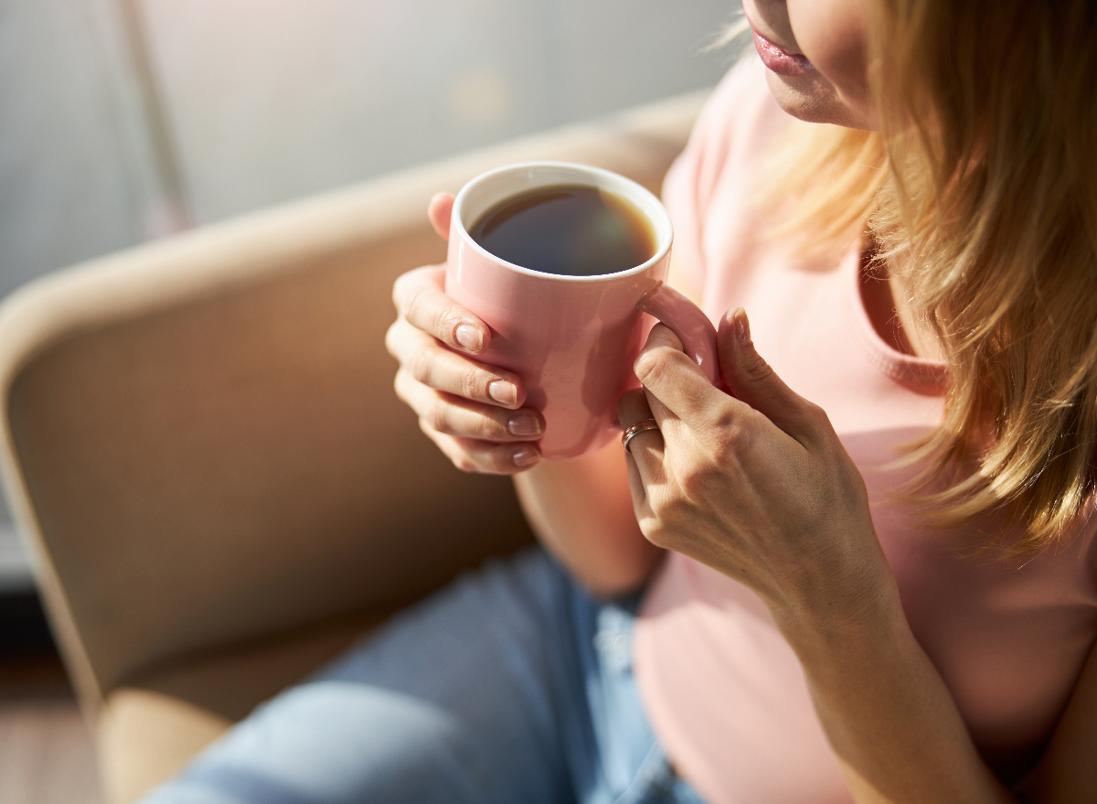 close-up mature woman in pink shirt holding pink mug of coffee, concept of how drinking coffee can help you lose weight