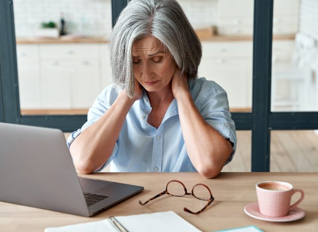 mature woman dealing with stiff neck, neck pain, doing neck stretches at her desk