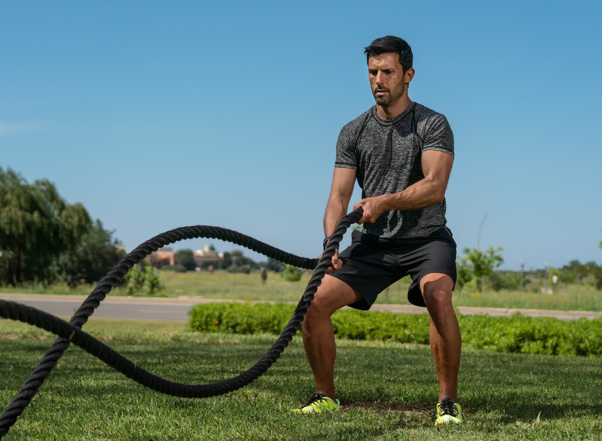 middle-aged man outdoors demonstrating battle ropes workout to get rid of hanging belly fat