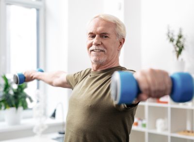 older man holding out dumbbells demonstrating arm-strengthening exercises for seniors