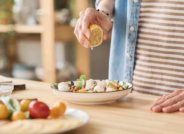 close-up hand squeezing lemon juice onto salad