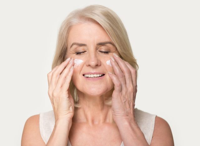 happy mature woman applying moisturizer on her face