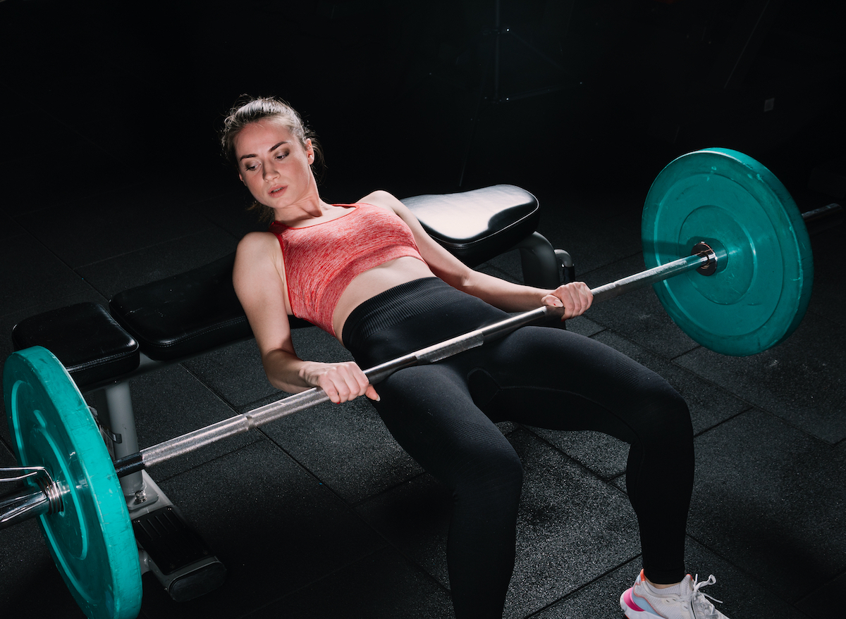 woman demonstrates how to do a hip thrust with a barbell