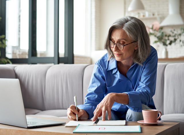 mature woman sitting on couch working, taking notes, concept of sedentary life leading to flat butt