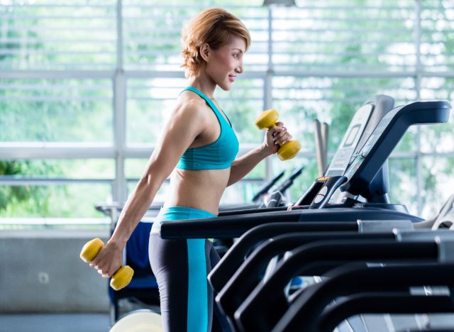 fitness woman doing incline cardio workout on treadmill holding dumbbells