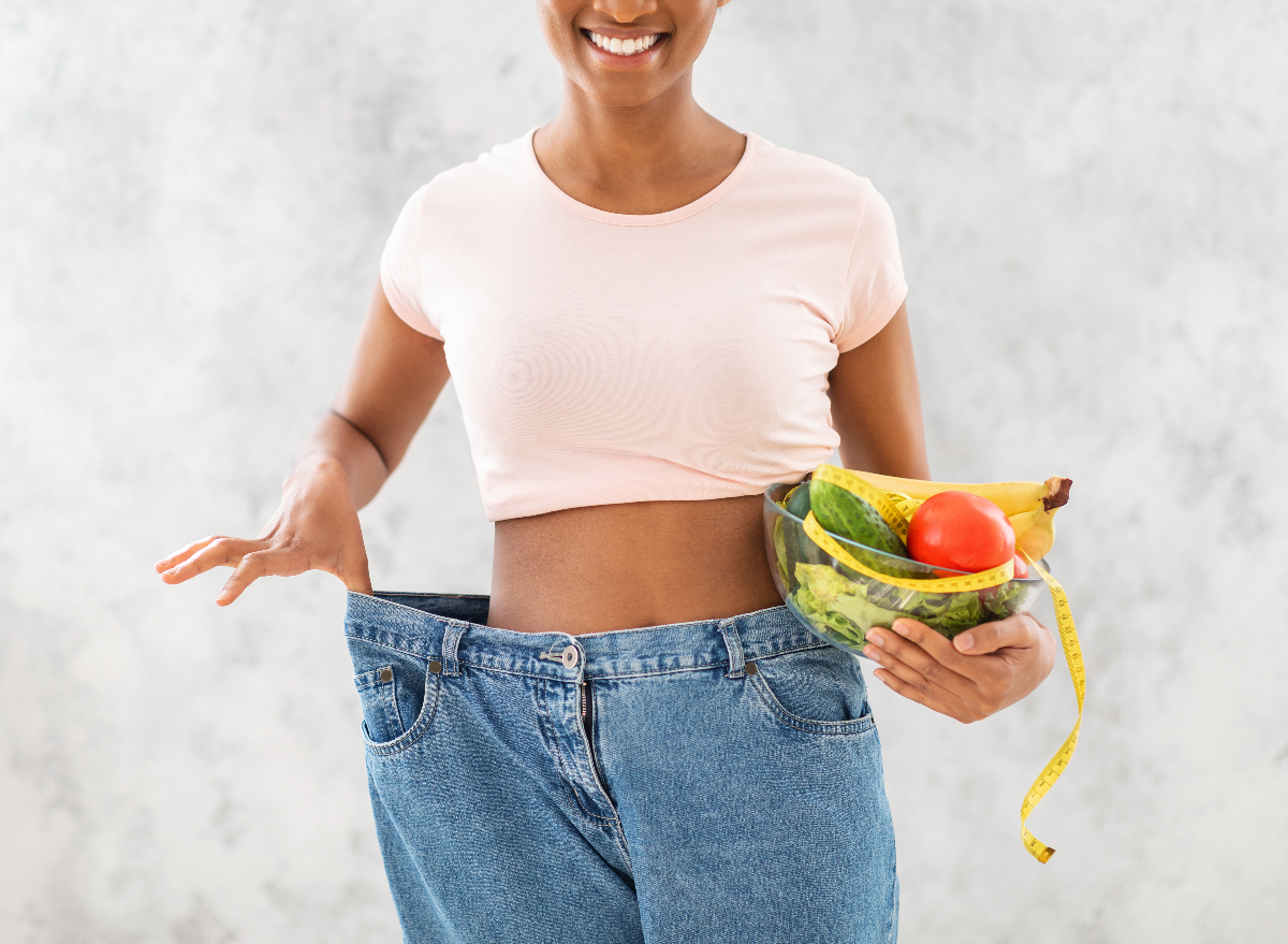 woman in baggy jeans holding bowl of fruits and veggies, weight loss tips concept