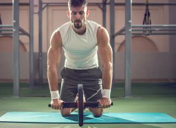 muscular man doing core-strengthening exercises ab wheel rollout