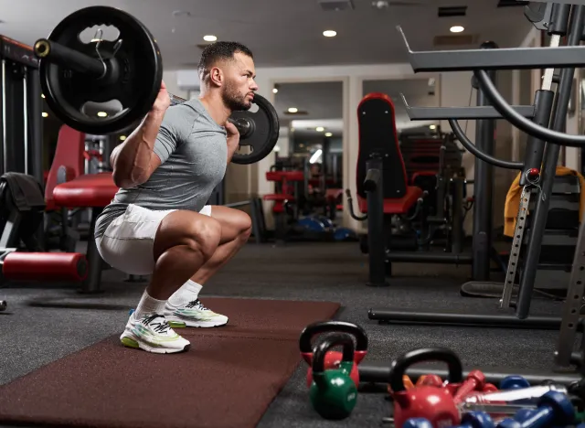 man doing a barbell back squat at the gym