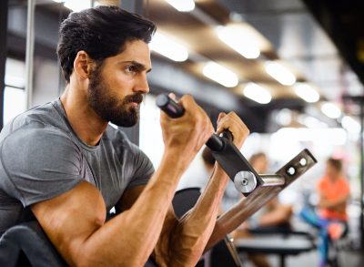 fit man performing arm exercise on machine to build muscle density and boost strength