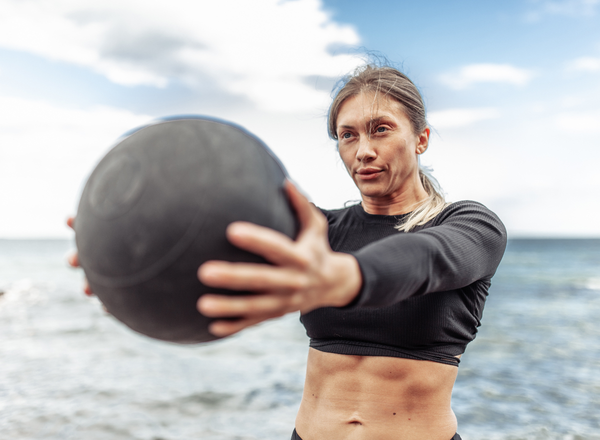 fit woman doing core-strengthening exercises with medicine ball at the beach