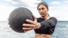 fit woman doing core-strengthening exercises with medicine ball at the beach