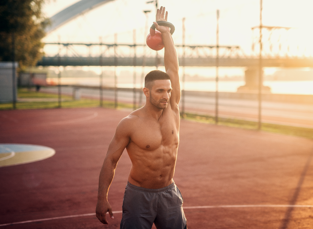 fit man holding kettlebell overhead during outdoor workout, concept of habits that kill workout progress