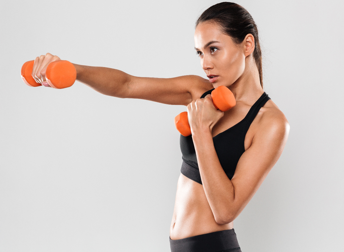 fit woman holding out orange dumbbells, concept of dumbbell exercises to lose weight in 30 days