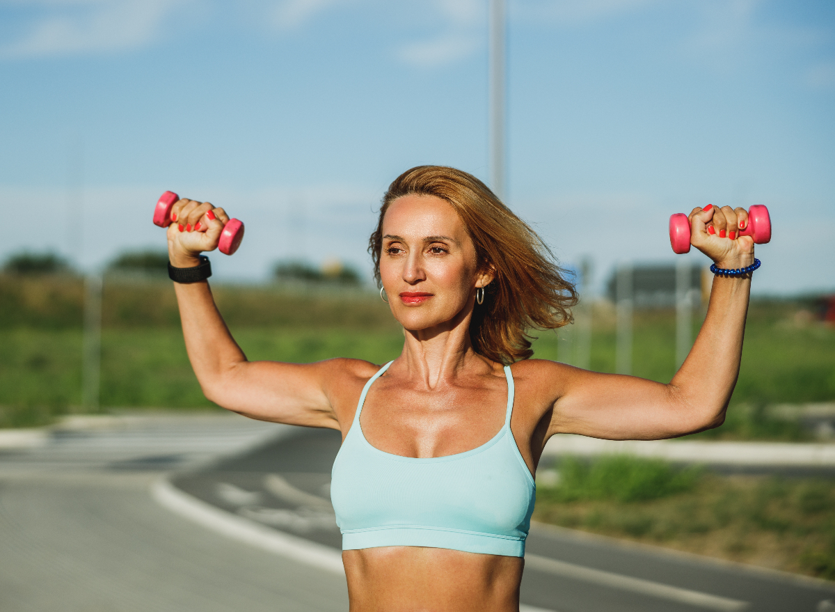 fit middle-aged woman holding up dumbbells outdoors, concept of strength exercises to stay fit