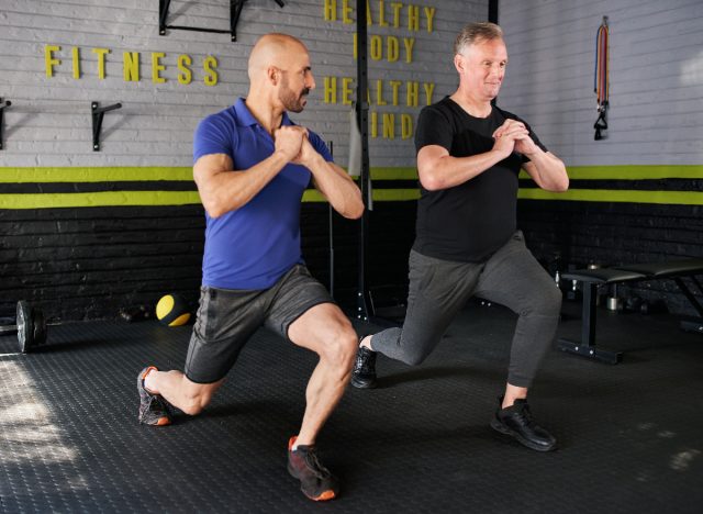 elderly man doing forward lunges with trainer at the gym