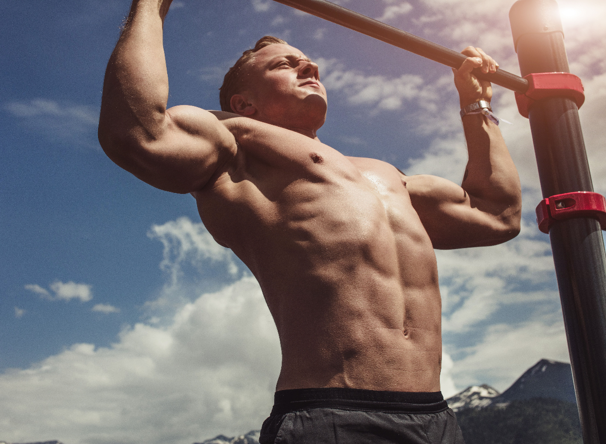 muscular man doing chin-ups outdoors to build size and strength