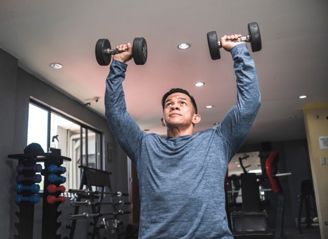 man doing dumbbell overhead presses, exercises to get rid of a dad belly