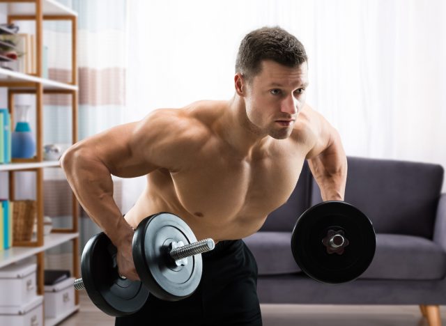 fit man lifting heavy dumbbells at home to build muscle density and boost strength