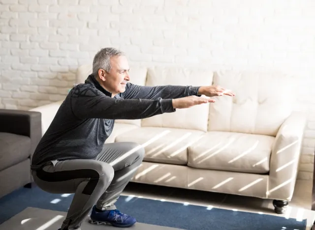 middle-aged man doing squats in living room, exercises for men to stay fit after 50