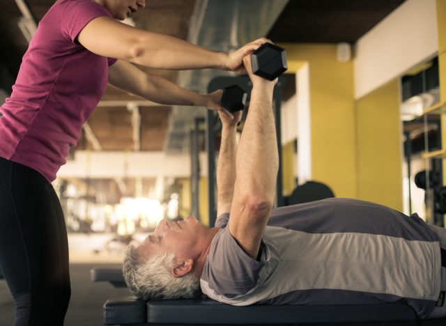 man lifting weights on bench with personal trainer at the gym