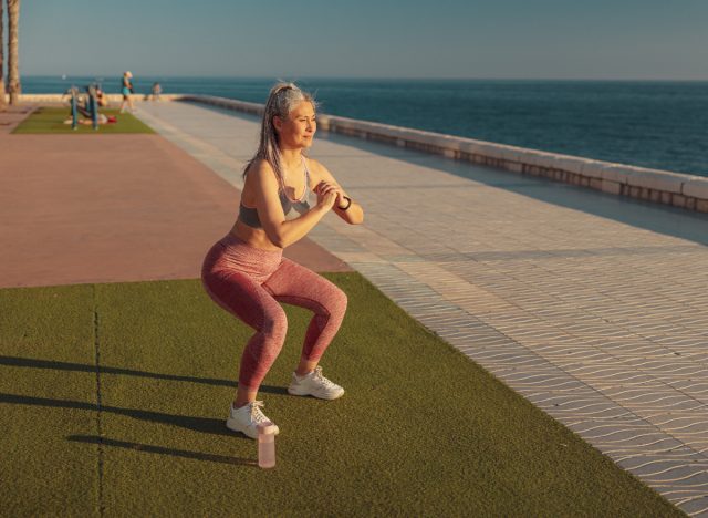 mature woman doing squats on turf by the water