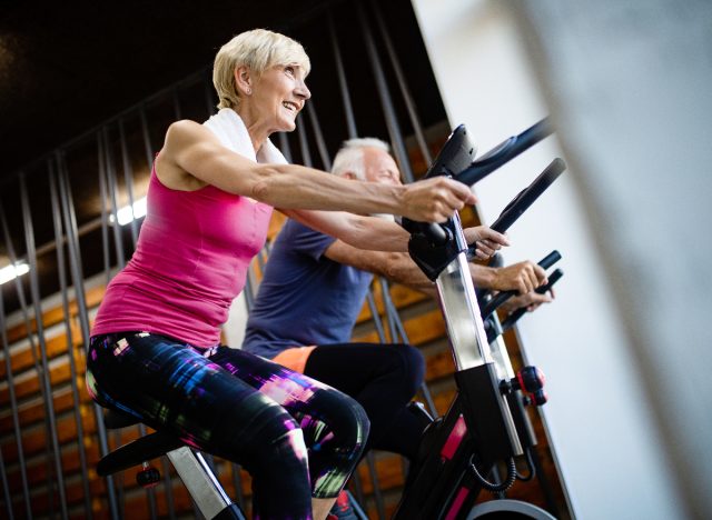 two older adults doing indoor cycling at the gym
