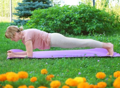 senior woman doing plank outdoors on yoga mat, demonstrating back-strengthening exercises for seniors