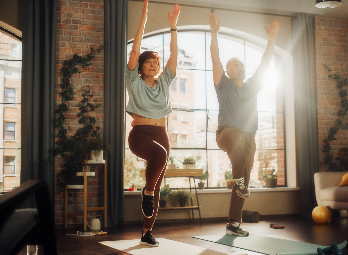 older couple demonstrating exercises for seniors to prevent falls, balancing on yoga mats in apartment
