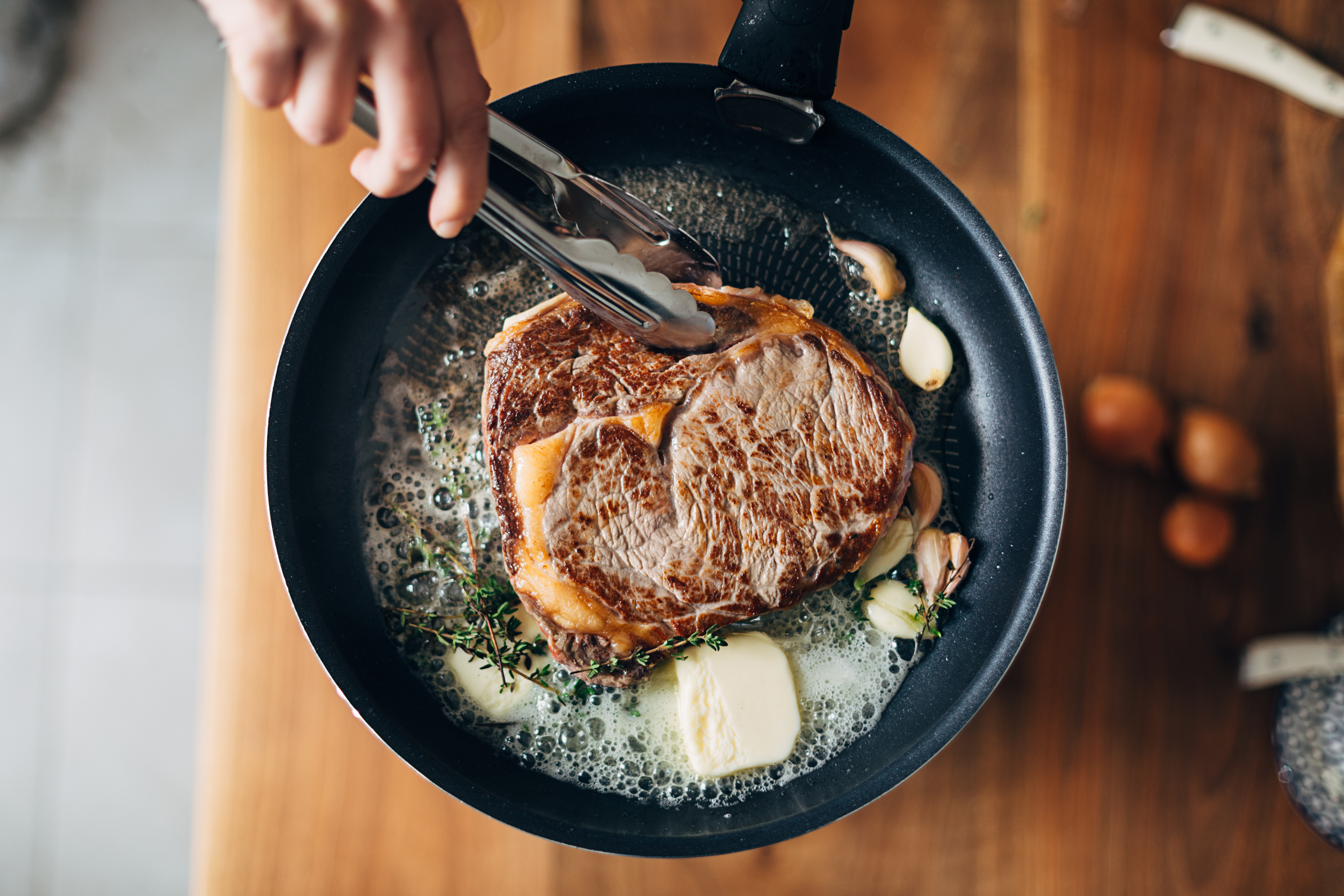 chef searing steak with butter and thyme