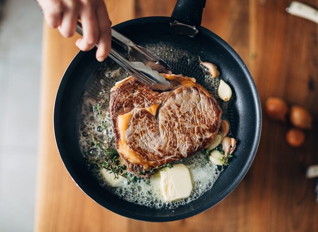 chef searing steak with butter and thyme