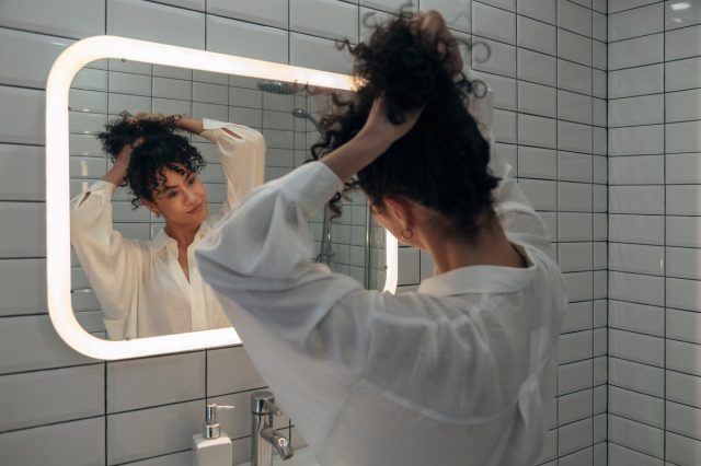 woman looking in the mirror and making her hair into a ponytail