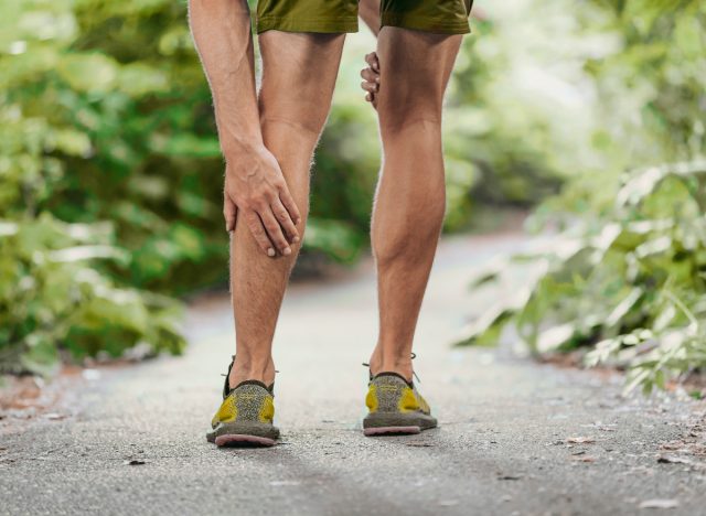 close-up man touching his sore leg while out on a walk