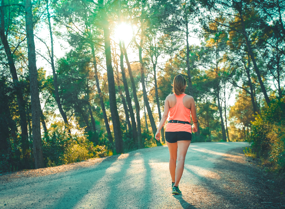 woman doing walking workout uphill on street with sunlight coming through trees
