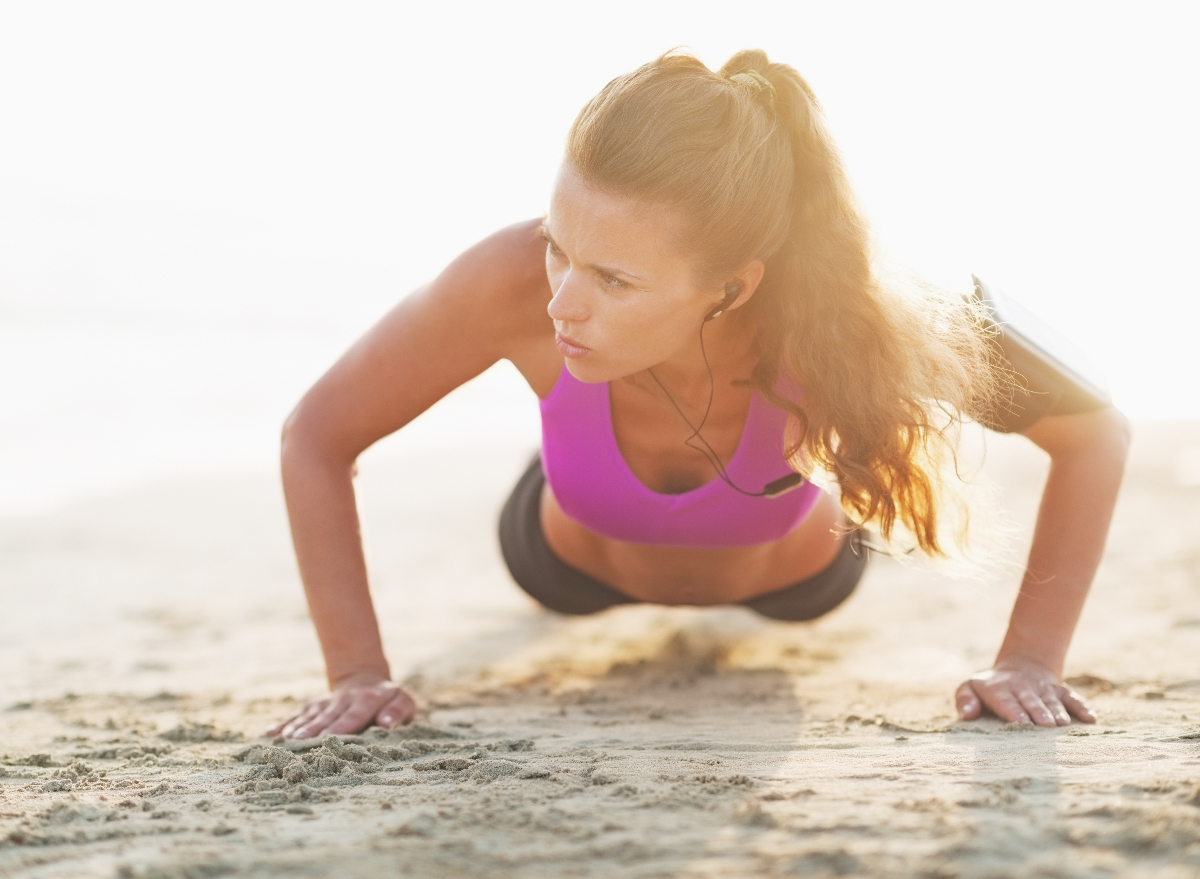 woman demonstrating bodyweight exercises, pushups on the beach to get rid of an apron belly