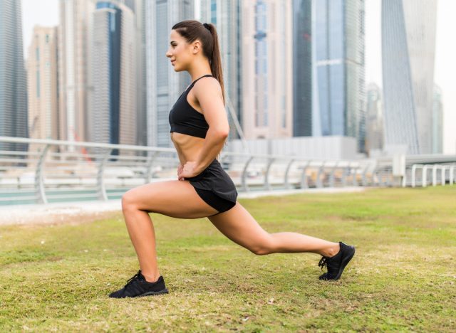 woman doing forward lunges exercise, city backdrop, part of full-body workout outdoors
