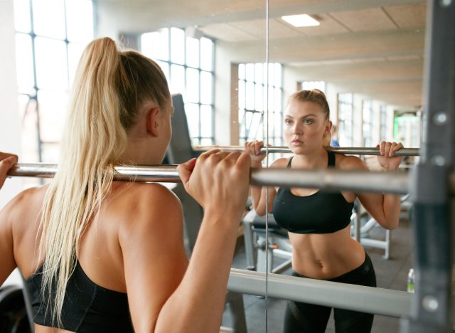 woman working out with barbell in mirror at gym, concept of bad fitness habits