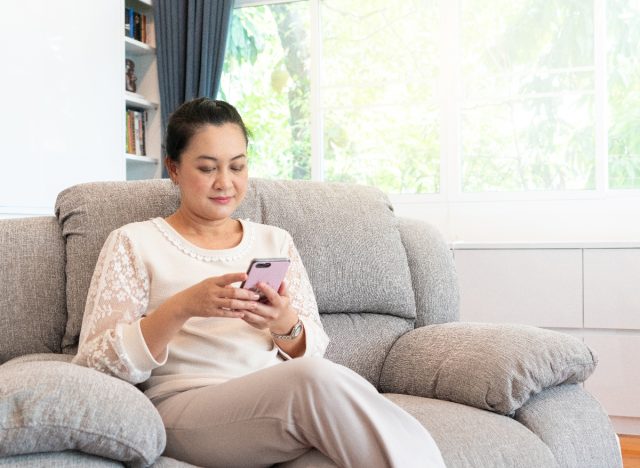 woman texting on her phone while sitting on couch instead of exercising, exercise habits that destroy your body