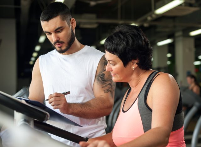 concept of middle-aged woman workout planning with trainer at gym