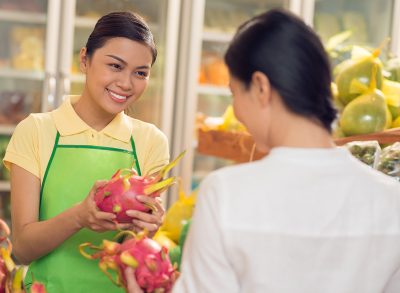 A saleswoman giving a ripe pitaya fruit to a supermarket customer.