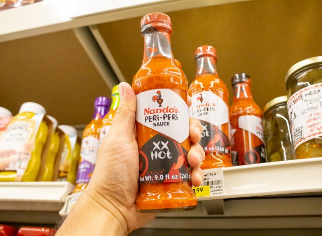 A hand holds a bottle of Nando's Peri-Peri Sauce at a local grocery store