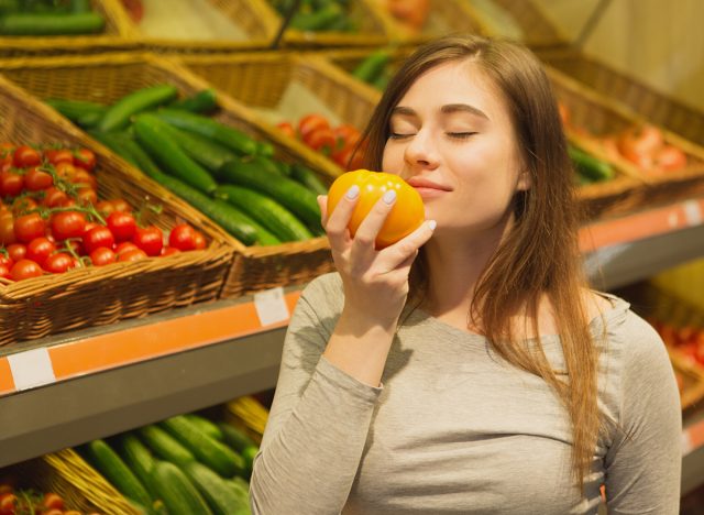Beautiful woman smelling a fresh tomato at the supermarket.
